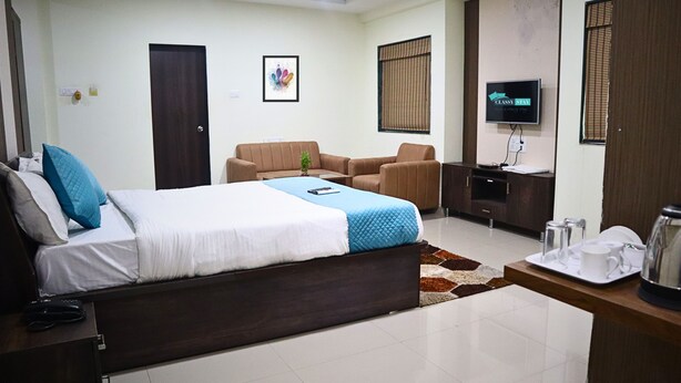 A hotel room with a bed, a sofa, a TV, and a coffee table with a kettle and cups. - Hotel Bramha inn (Pune)