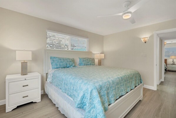 A bedroom with a bed, nightstands, a ceiling fan, and a window with blinds.