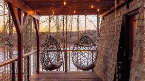 Une terrasse en bois avec deux fauteuils suspendus et une porte en bois.