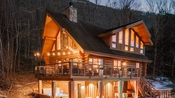 Une cabane en rondins à deux étages, dotée d’un balcon, d’une cheminée et d’une terrasse.