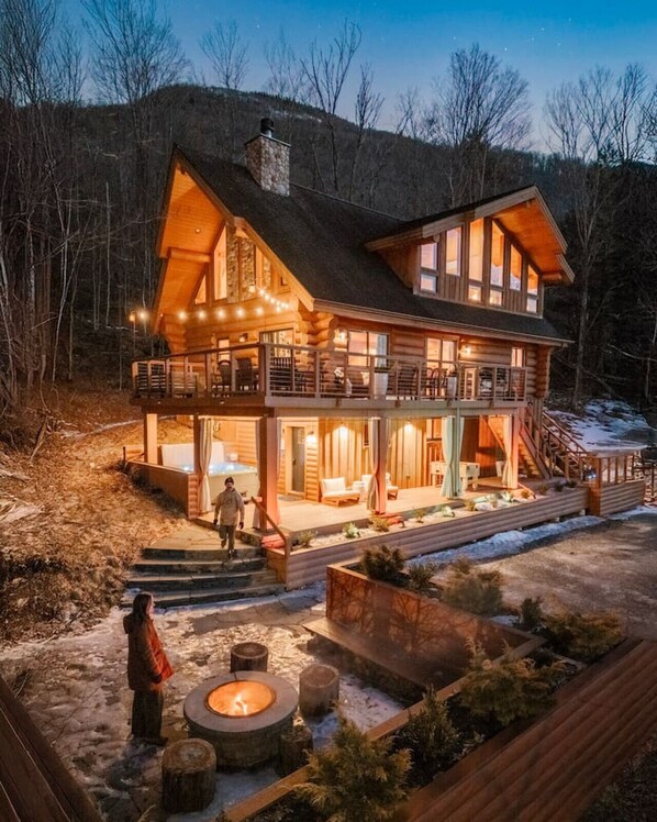 A two-story log cabin with a balcony, a fireplace, and a deck area.
