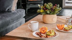 Une pièce chaleureuse avec un décor intérieur en bois, une cheminée, un canapé, une table basse avec un petit-déjeuner, et une fenêtre.