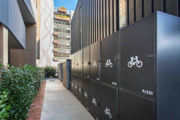 Bike storage area with numbered lockers and a pathway leading to a contemporary building.