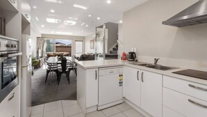 Una cocina moderna con armarios blancos, extractor de acero inoxidable y un comedor con mesa y sillas.