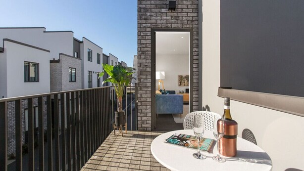 Een balkon met een betegelde vloer, een tafel met een tijdschrift, een fles en een stoel.