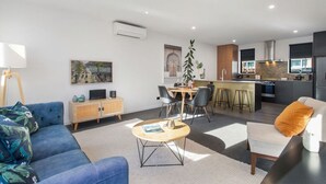 Een moderne woonkamer met een blauwe bank, een bijzettafeltje en een eethoek, met een keuken op de achtergrond.
