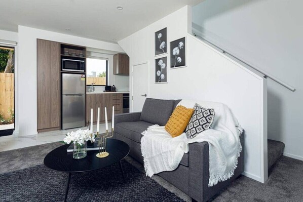 A modern living room with a grey sofa, a black coffee table, and a staircase.