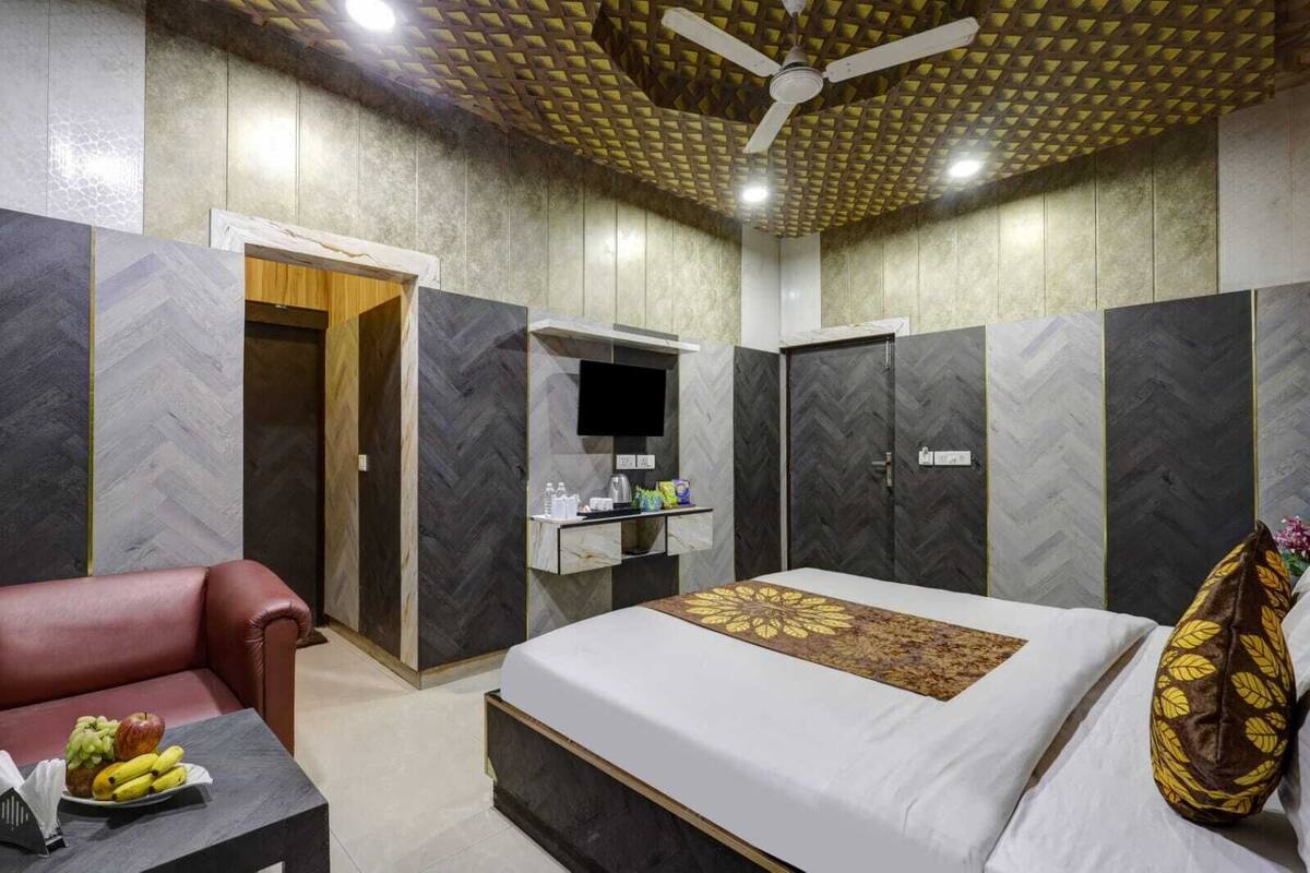 A modern hotel room with a large bed, a seating area with a table, a TV, and a wardrobe.