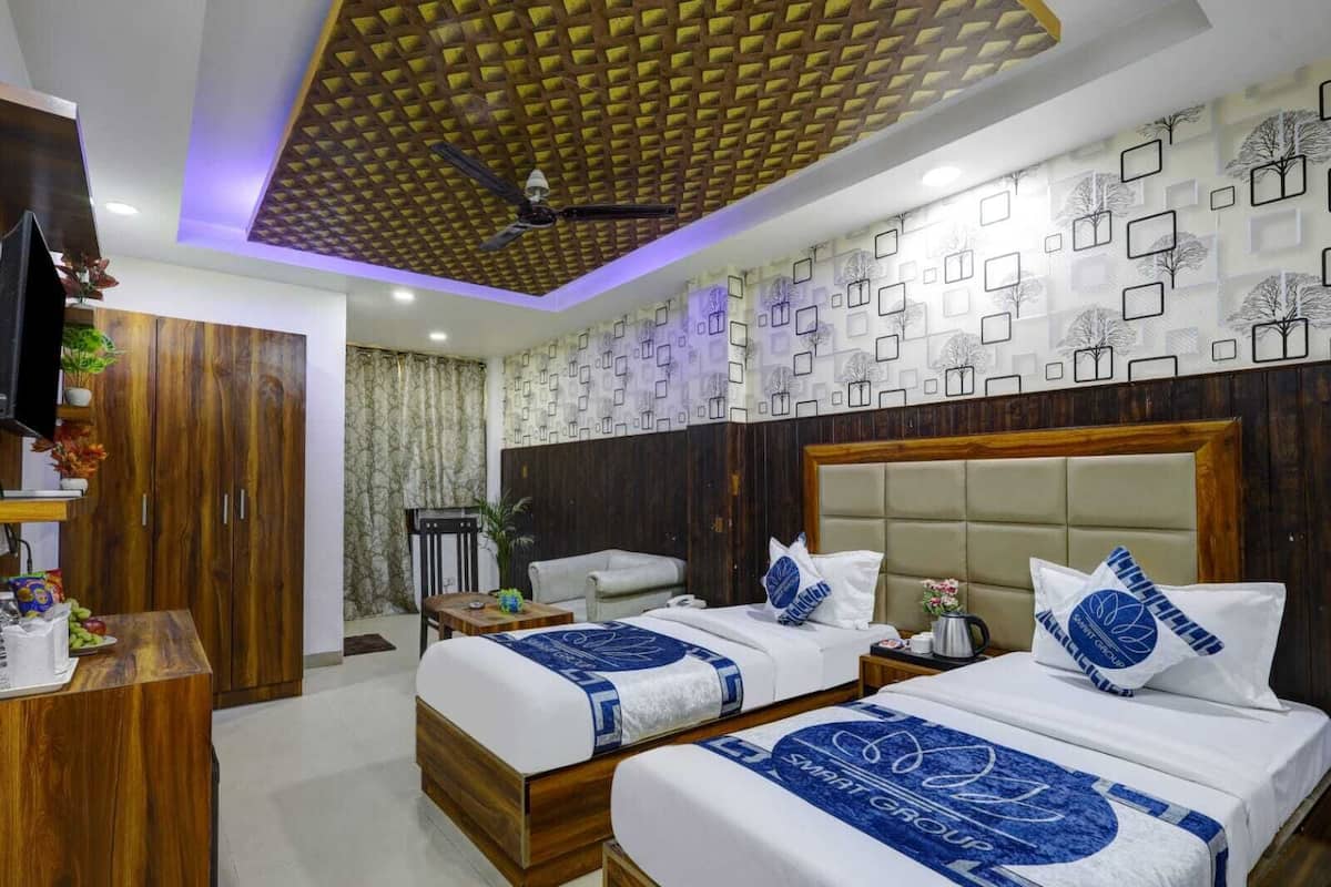 A hotel room with two beds, a wooden wardrobe, a desk, and a ceiling fan.