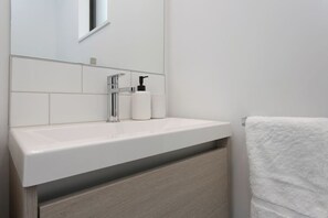 A modern bathroom with a white sink, chrome faucet, and a towel hanging on the wall.