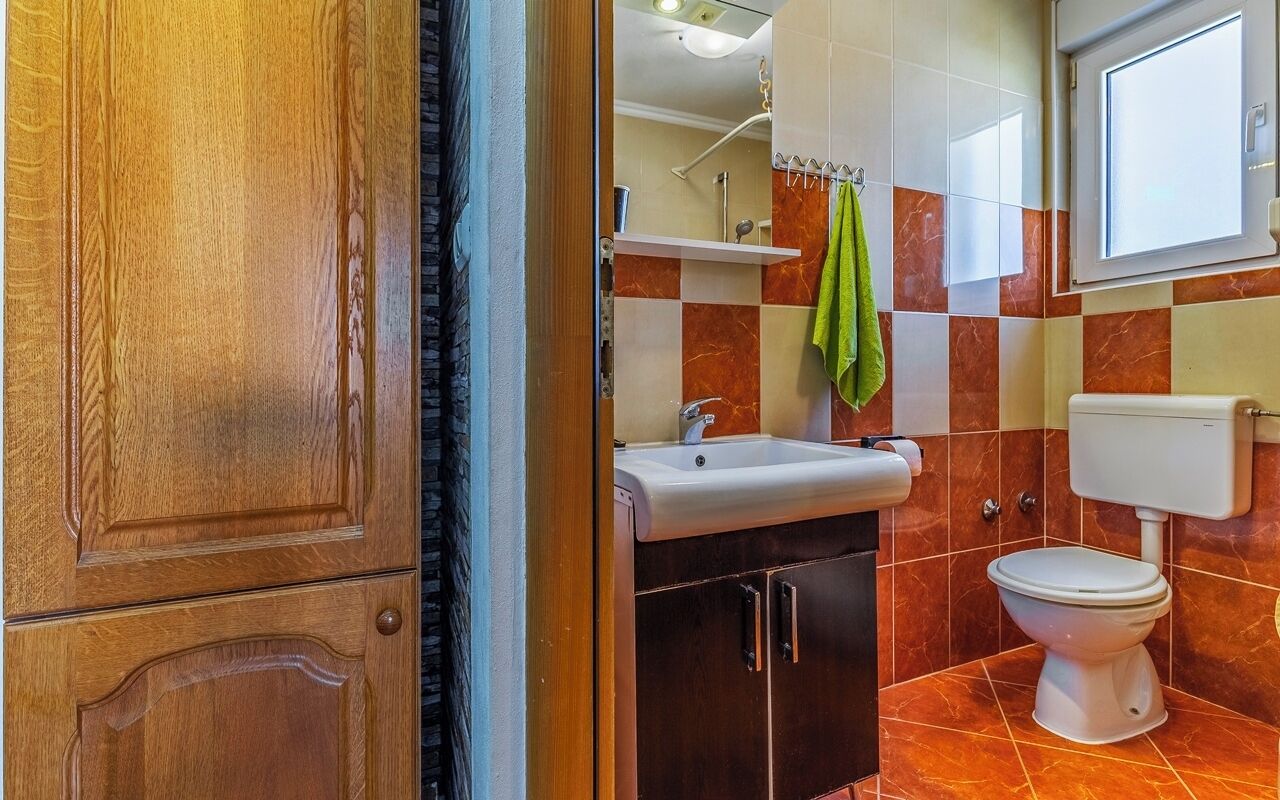 A bathroom with a wooden door, a sink, a toilet, and a mirror.