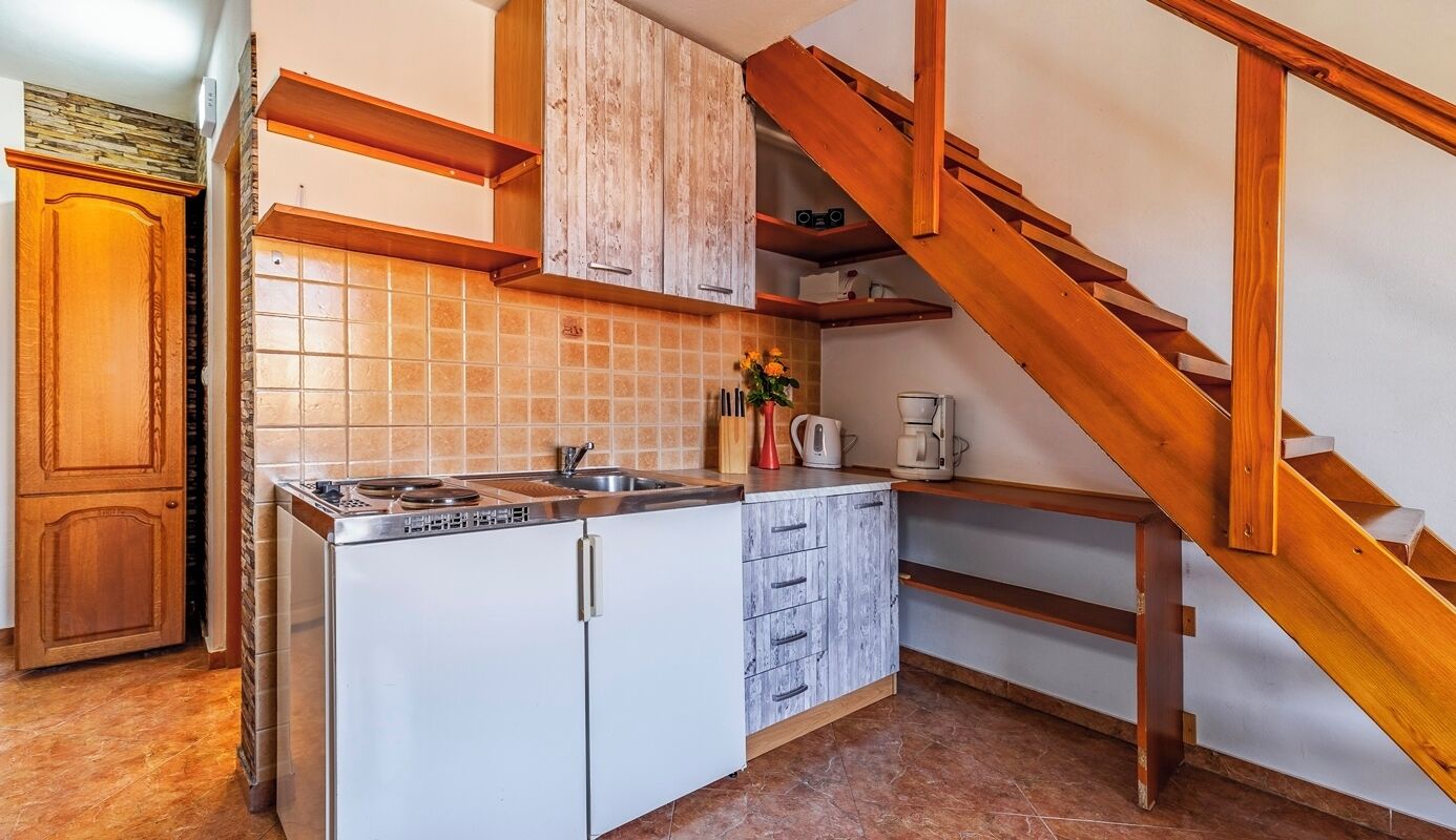 Una cocina con estufa integrada, armarios blancos, una escalera de madera y un salpicadero de azulejos.