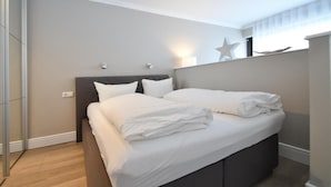 A neatly made bed with white linens, a dark headboard, and a wall-mounted star decoration. - Vacation apartment Bude 16 (Norderney)