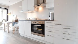 A modern kitchen with white cabinetry, a stainless steel oven, and a built-in range hood. - Vacation apartment Bude 16 (Norderney)