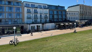 A modern building with multiple floors, large windows, and balconies. There is a café with outdoor seating and umbrellas. - Vacation apartment Gezwitschert (Norderney)