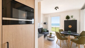 A modern kitchen with a Siemens oven, a dining area with a round table and chairs, a sofa, and a view of the ocean. - Vacation apartment Gezwitschert (Norderney)