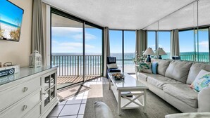 Un salon spacieux avec un grand balcon donnant sur l’océan, un canapé confortable, une table basse et un téléviseur.