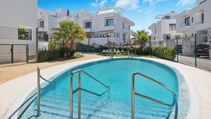 A modern pool area with clear blue water, surrounded by white buildings and palm trees. - WHITE HOUSE : Charming & spacious Villa, Big terrace with sea & mountain views . (Fuengirola)
