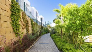 A paved pathway flanked by lush greenery and a stone wall with climbing plants. - WHITE HOUSE : Charming & spacious Villa, Big terrace with sea & mountain views . (Fuengirola)