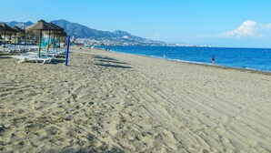 A beach with sun loungers and umbrellas, a clear sky, and mountains in the background. - WHITE HOUSE : Charming & spacious Villa, Big terrace with sea & mountain views . (Fuengirola)