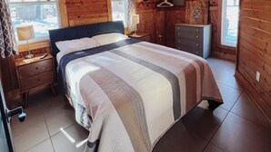 A wooden cabin bedroom with a bed, nightstands, a dresser, and a TV mounted on the wall. -  Cabin on private beach on a lake near Brainerd! 2 bedrooms, sleeps 7! (Brainerd)