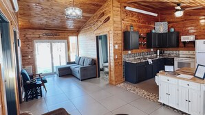 A spacious living area with a wooden ceiling, a sofa, a coffee table, and a kitchen area with cabinets and a microwave. -  Cabin on private beach on a lake near Brainerd! 2 bedrooms, sleeps 7! (Brainerd)