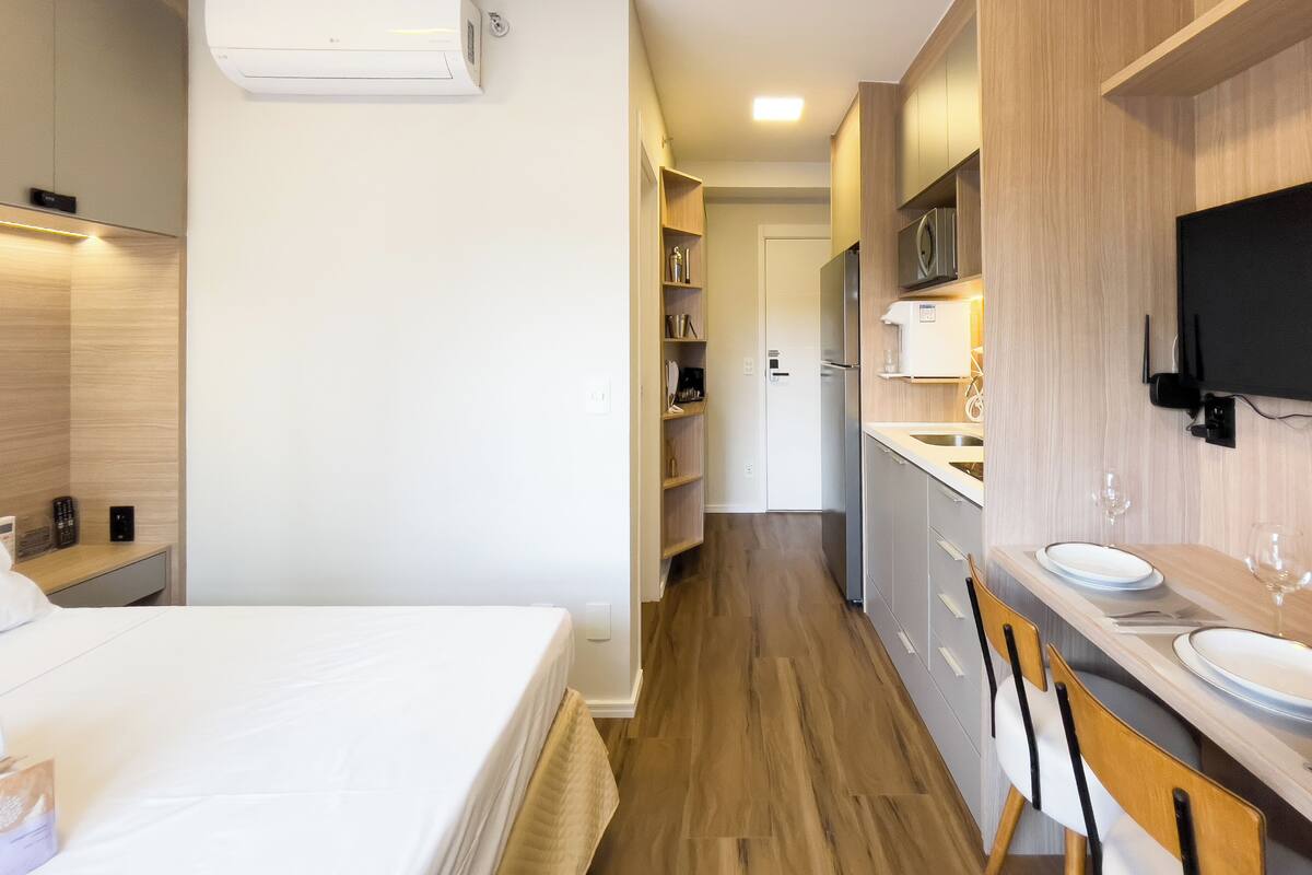 Une chambre d’hôtel moderne équipée d’un lit, d’une kitchenette et d’un téléviseur fixé au mur.