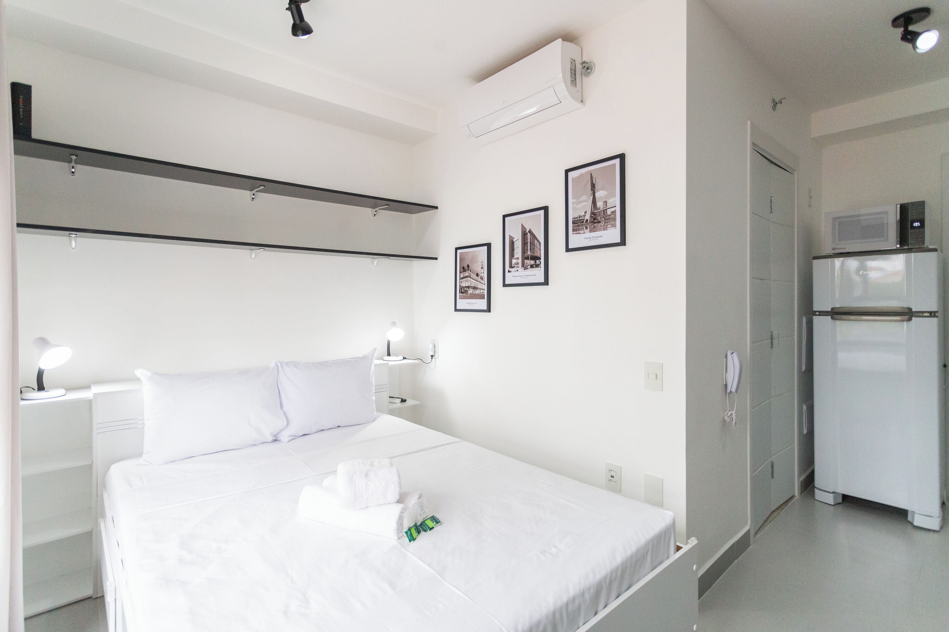 Une chambre d’hôtel avec un lit, des tables de chevet, un four à micro-ondes et des tableaux encadrés au mur.