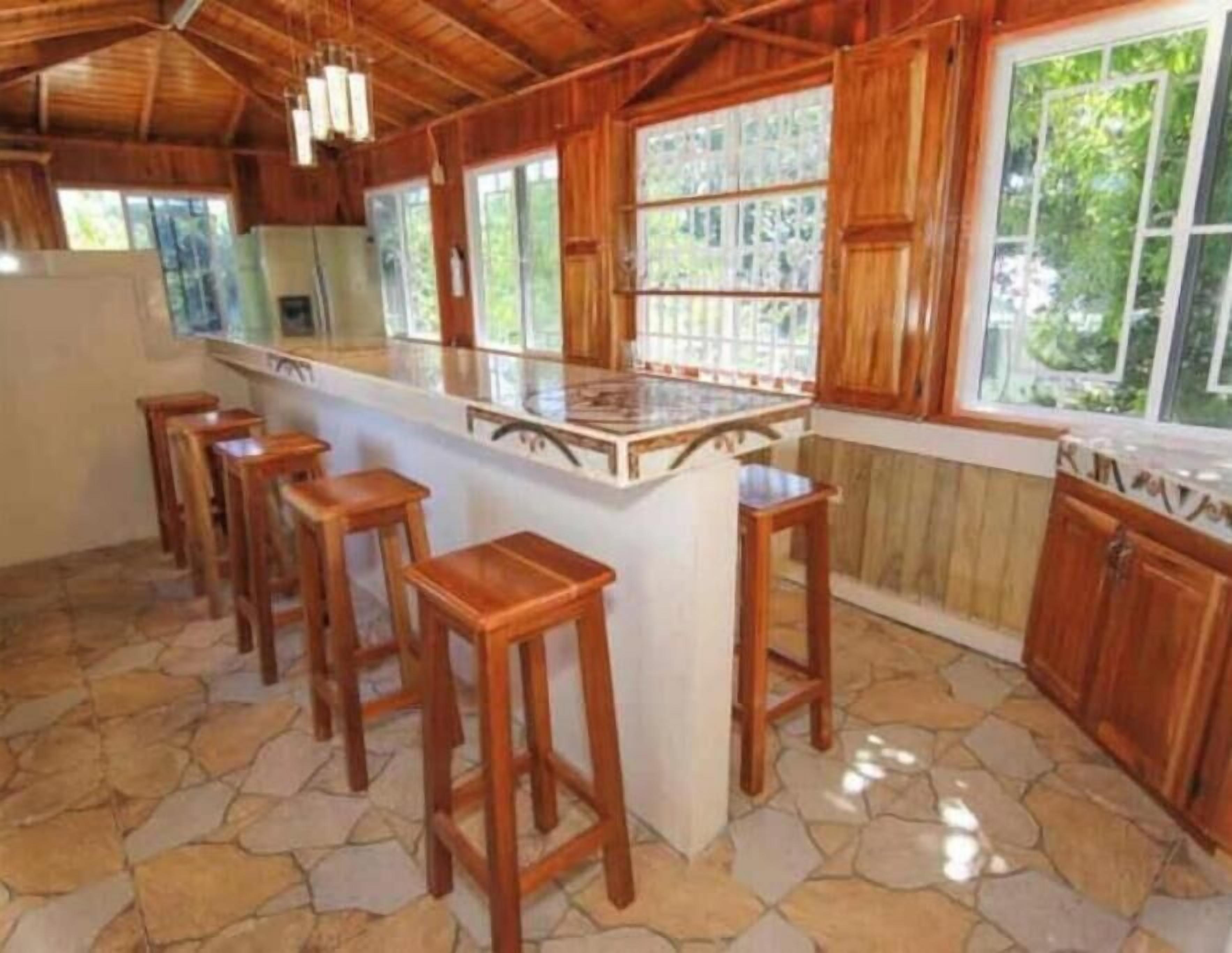 A kitchen with a central island, wooden stools, and large windows.