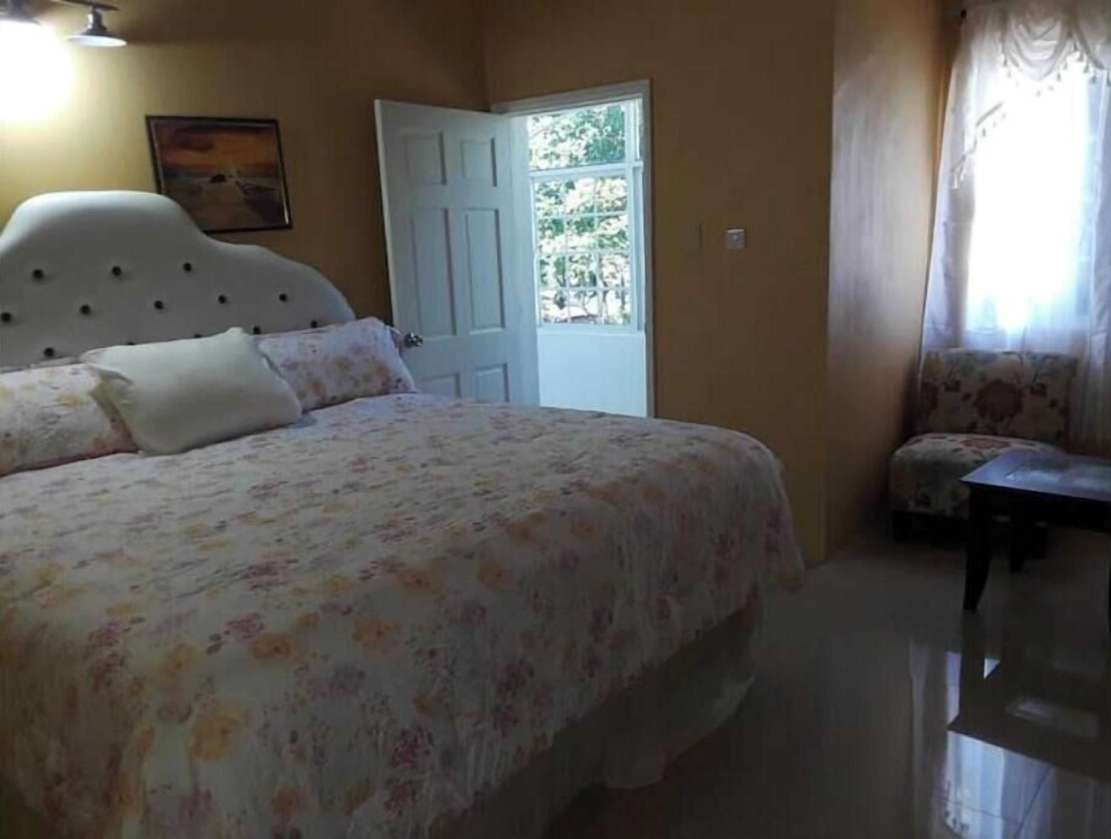 A bedroom with a bed, a chair, a door, and a painting on the wall.