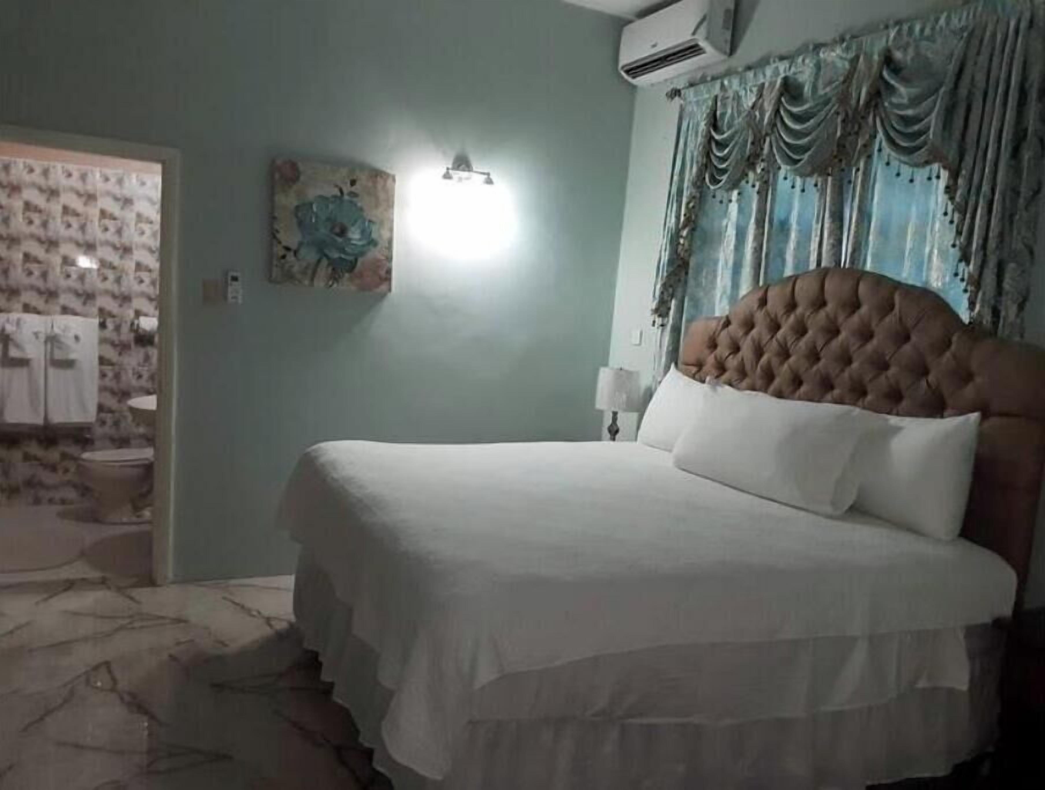 A bedroom with a large bed, a nightstand, a wall-mounted lamp, and a painting.
