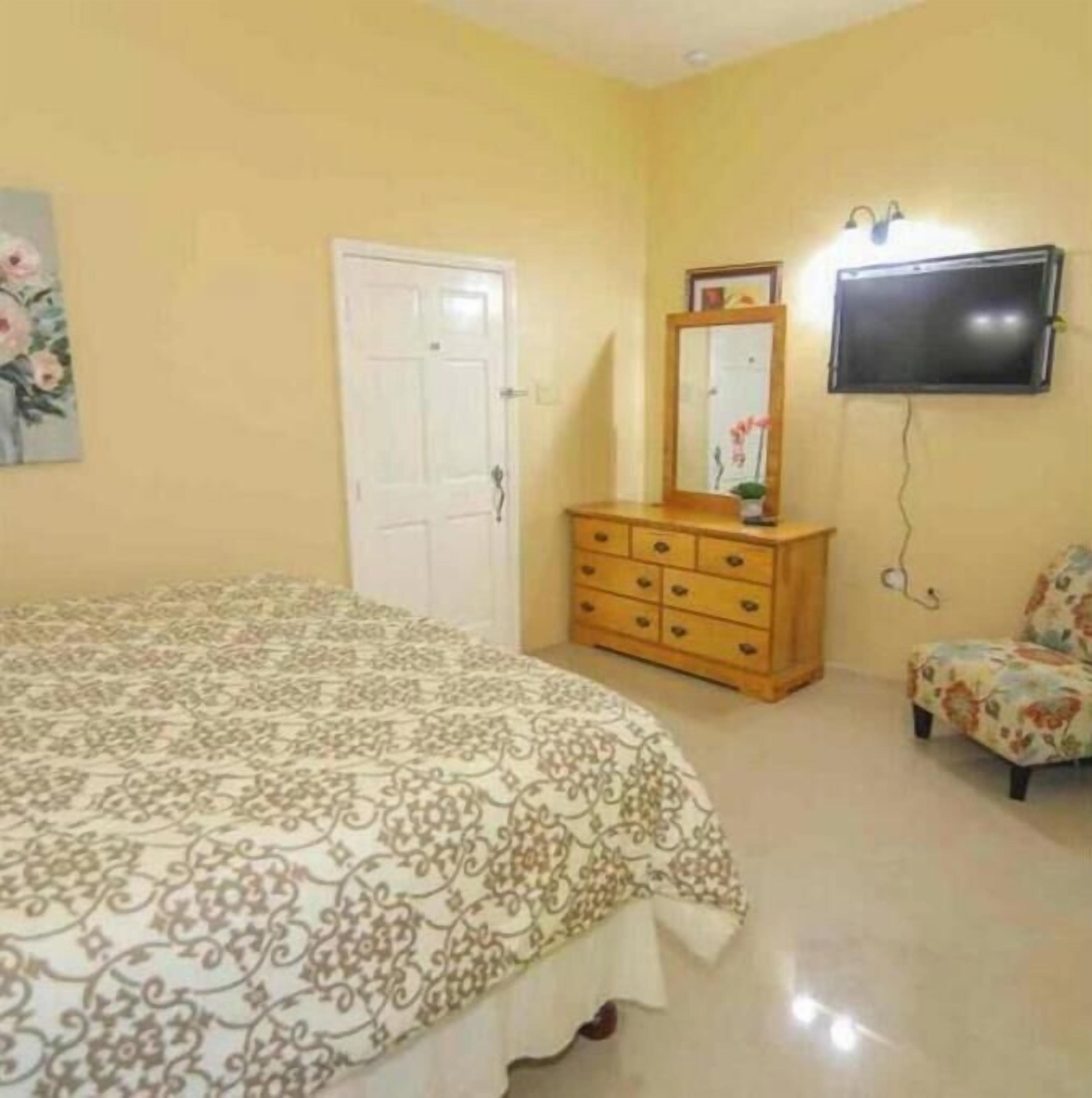 A bedroom with a bed, a dresser, a chair, a TV, and a door.