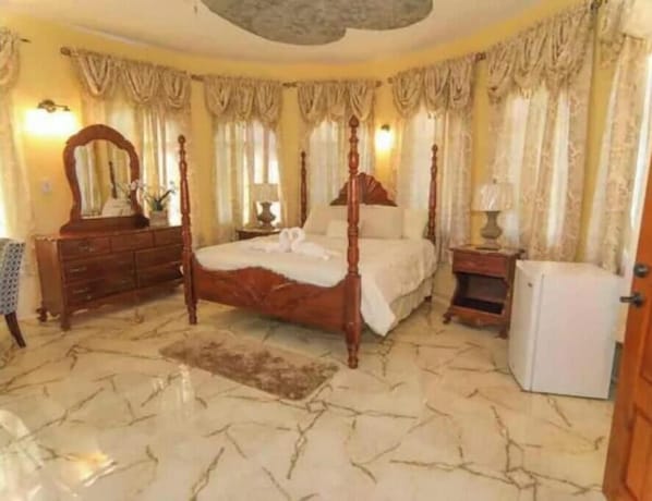 A bedroom with a four-poster bed, a dresser, a mirror, a nightstand, and a refrigerator.