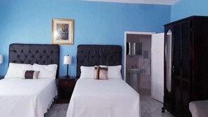 A hotel room with two beds, a ceiling fan, a framed picture on the wall, and a wardrobe.