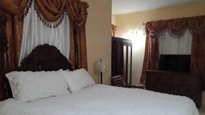 A bedroom with a large bed, a wardrobe, a television, and curtains.