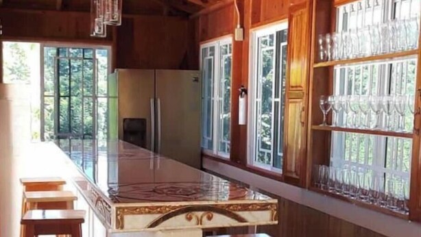 A kitchen with a long countertop, wooden stools, and a glass display case.