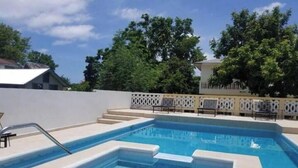 A rectangular swimming pool with steps leading into it, surrounded by a white fence and trees in the background.