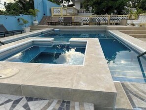 Una piscina rectangular con un pequeño jacuzzi en el centro, rodeada por una terraza de baldosas.