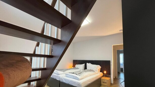Un dormitorio moderno con una cama grande, una escalera de madera y una mesita de noche con una lámpara.