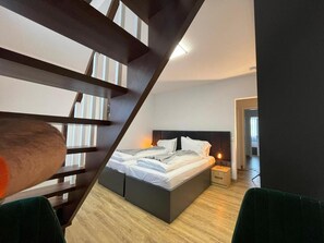 A modern bedroom with a large bed, a wooden staircase, and a nightstand with a lamp. - Haven - Hotel Dona (Bergisch Gladbach)