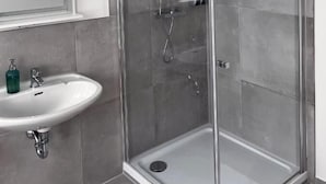 Un baño moderno con cabina de ducha de vidrio, un lavabo blanco con dispensador de jabón y un espejo sobre el lavabo.