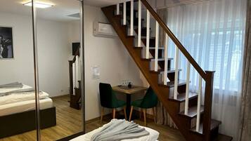 A bedroom with a wooden staircase, a bed, a desk with two chairs, and a large mirror.