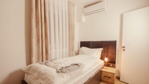 Una cama bien hecha con cabecera, una mesita de noche con lámpara y un equipo de aire acondicionado en la pared.