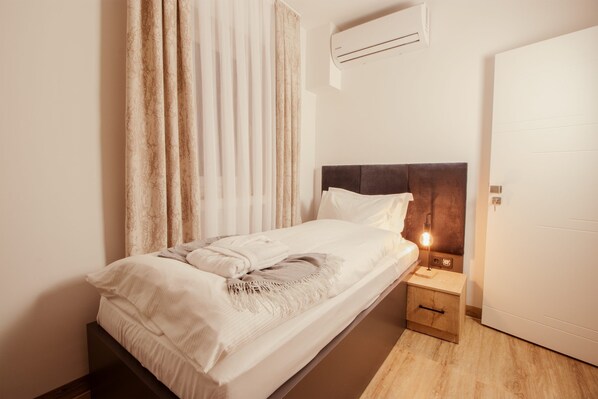 Un lit bien fait, avec une tête de lit, une table de chevet avec une lampe et un appareil de climatisation fixé au mur.