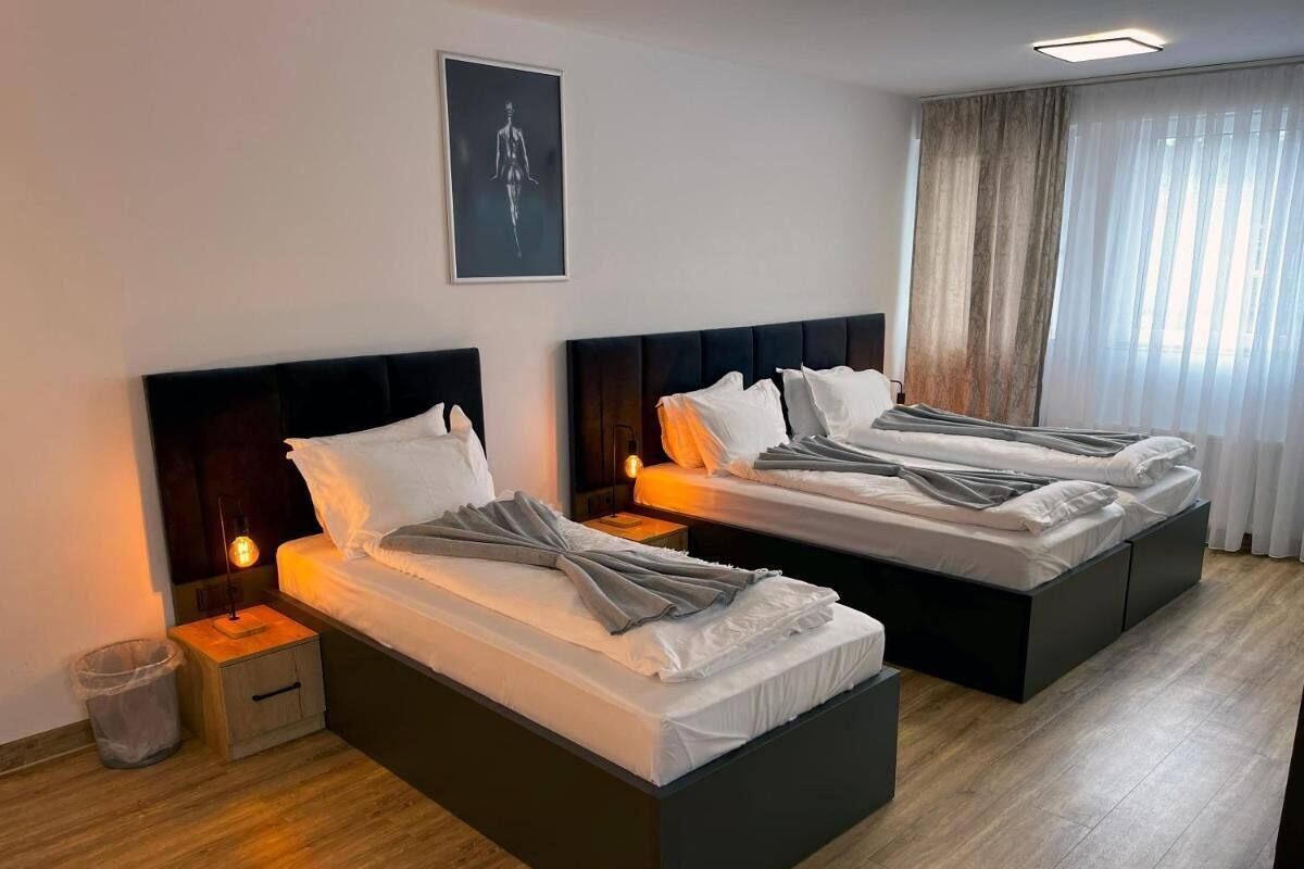 Quarto de hotel com duas camas, cada uma com cabeceira, mesas de cabeceira e luz noturna.