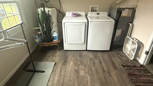 A laundry area with two white washing machines, a drying rack, a radiator, and a window with a view of the outside.