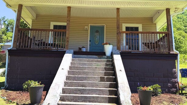 A two-story house with a front porch, a blue door, and a small garden area with potted plants.