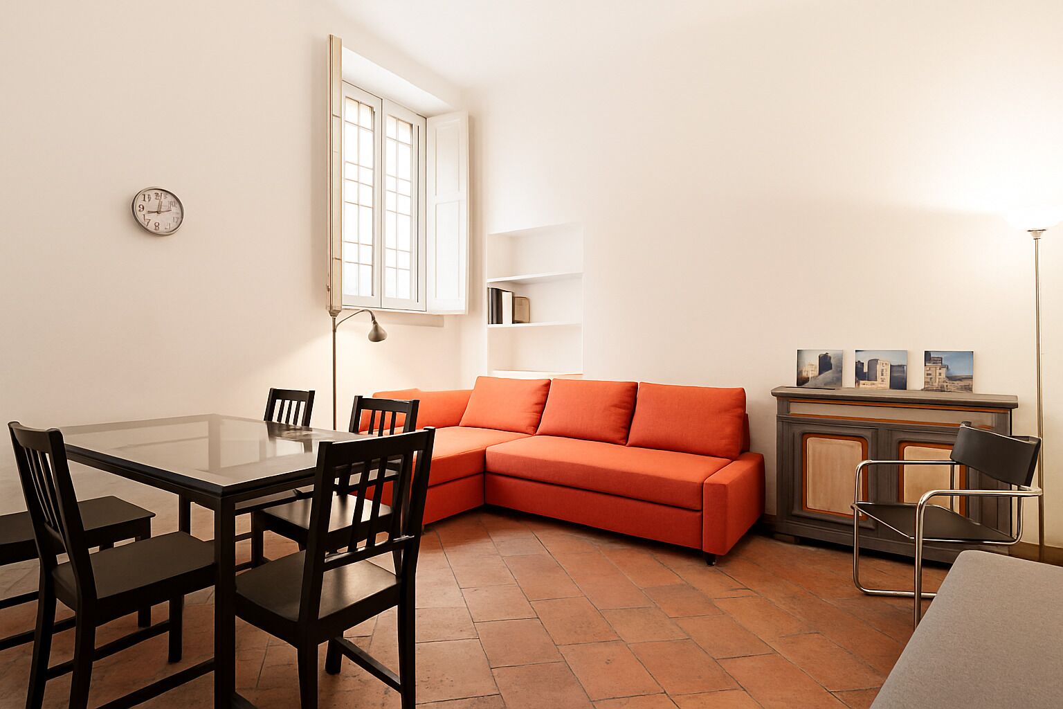 A compact living space with a dining area, a sofa, a cabinet, and a clock on the wall.
