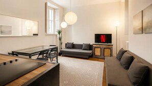 Ett modernt vardagsrum med en soffa, en tv, ett matbord och ett stort fönster.