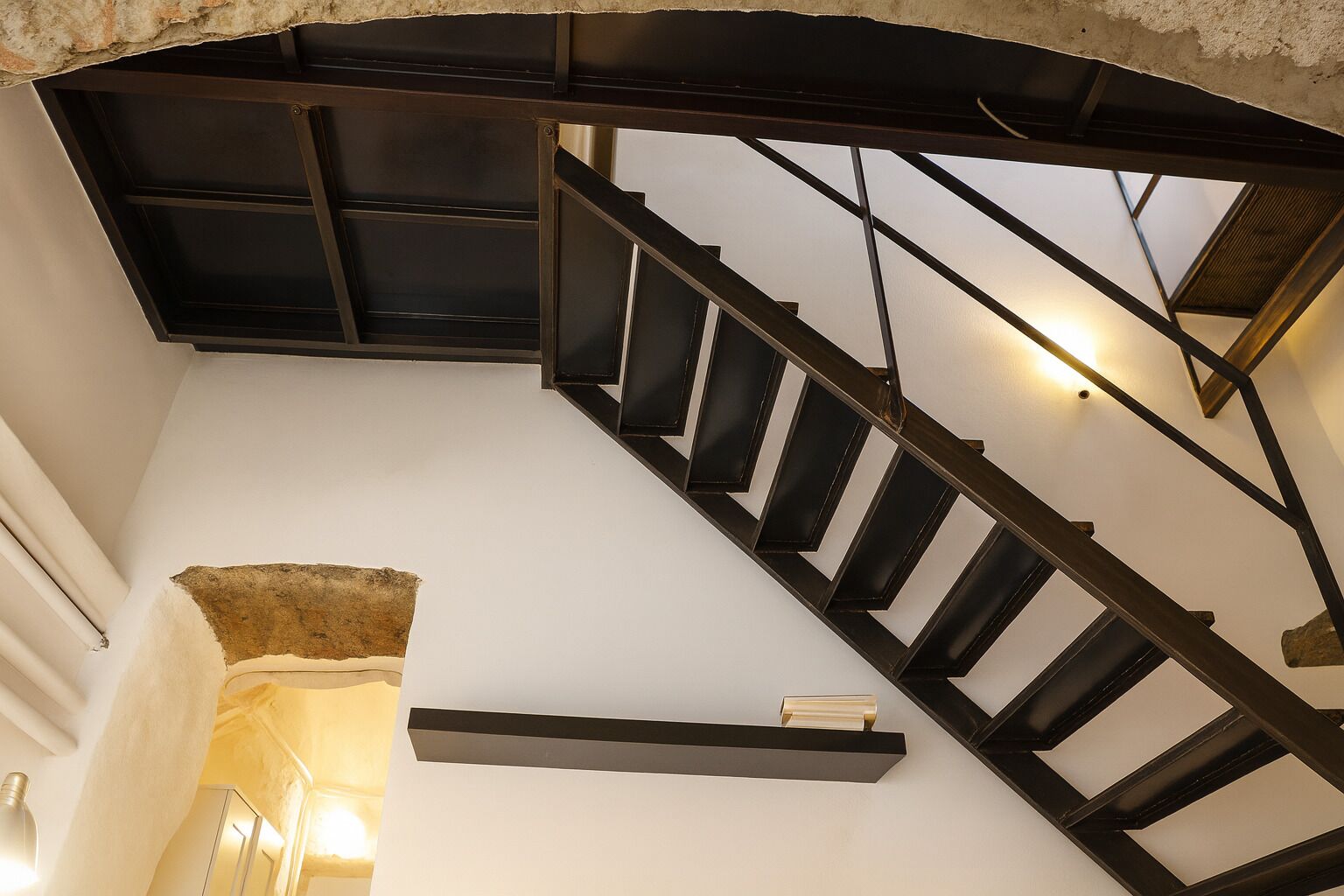 Un escalier moderne avec une structure en métal noir et un mur blanc.